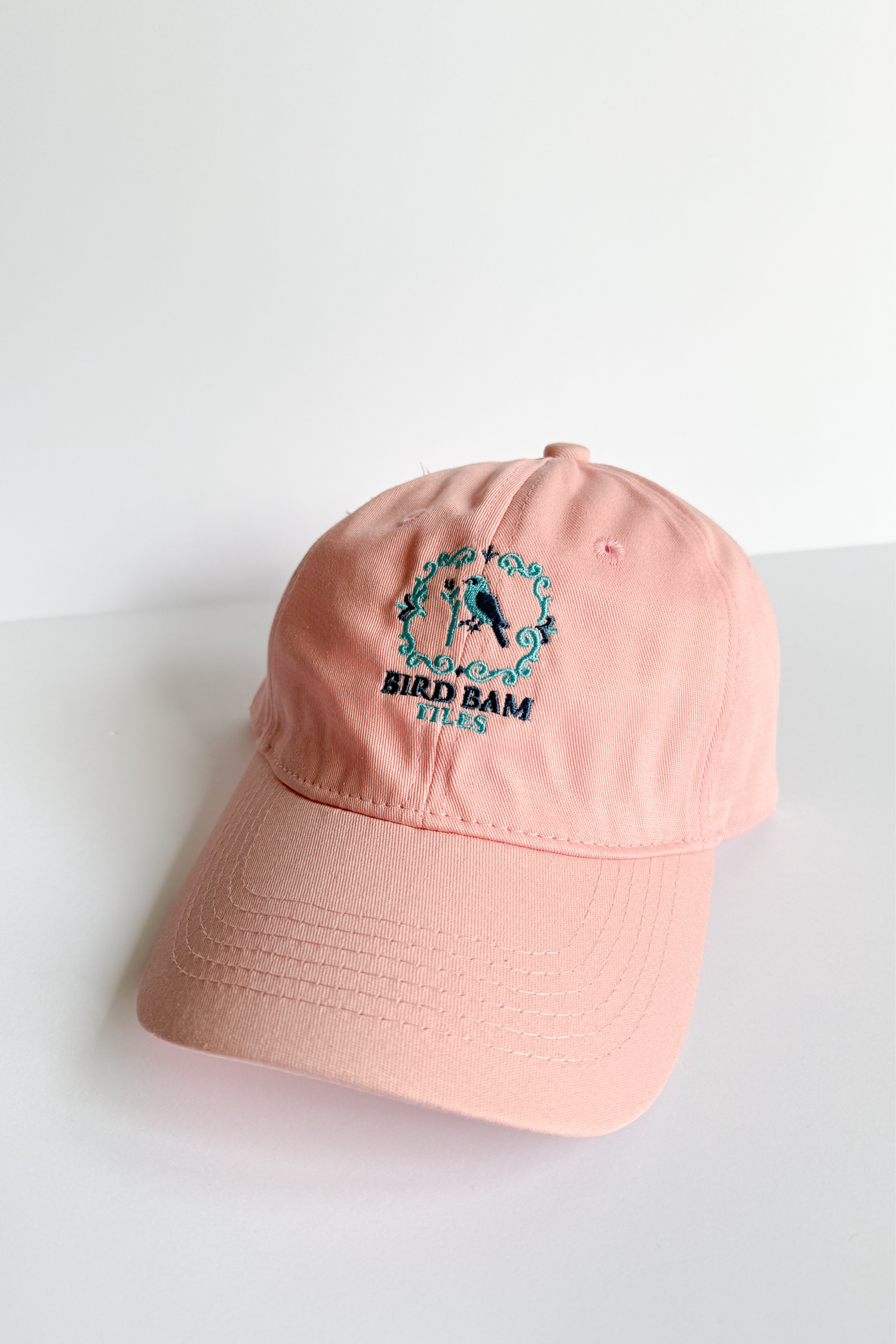 Peachy pink baseball hat with Bird Bam Logo embroidered on a white background