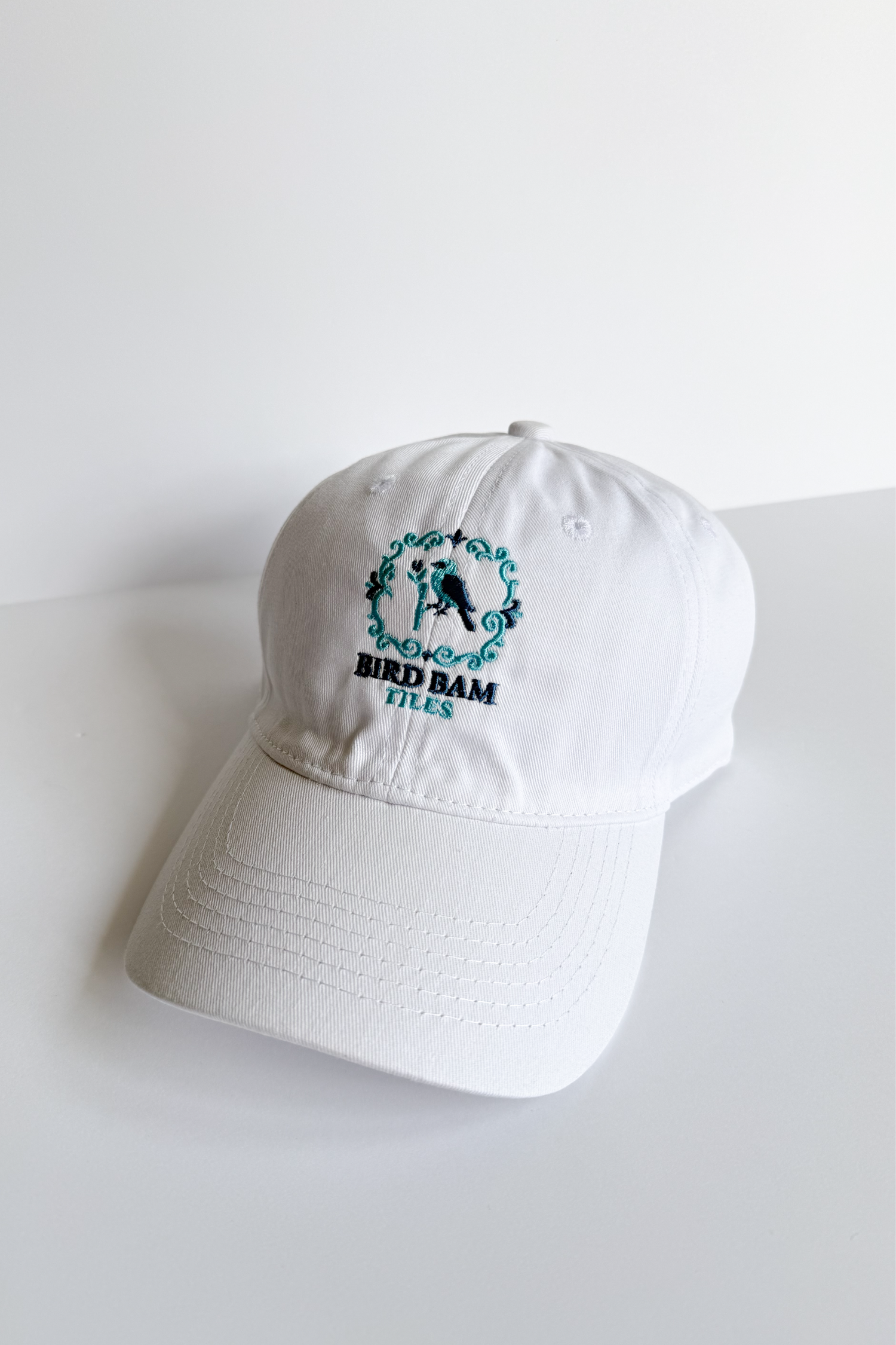 White baseball hat embroidered with 2-toned blue Bird Bam Tiles logo on a white background