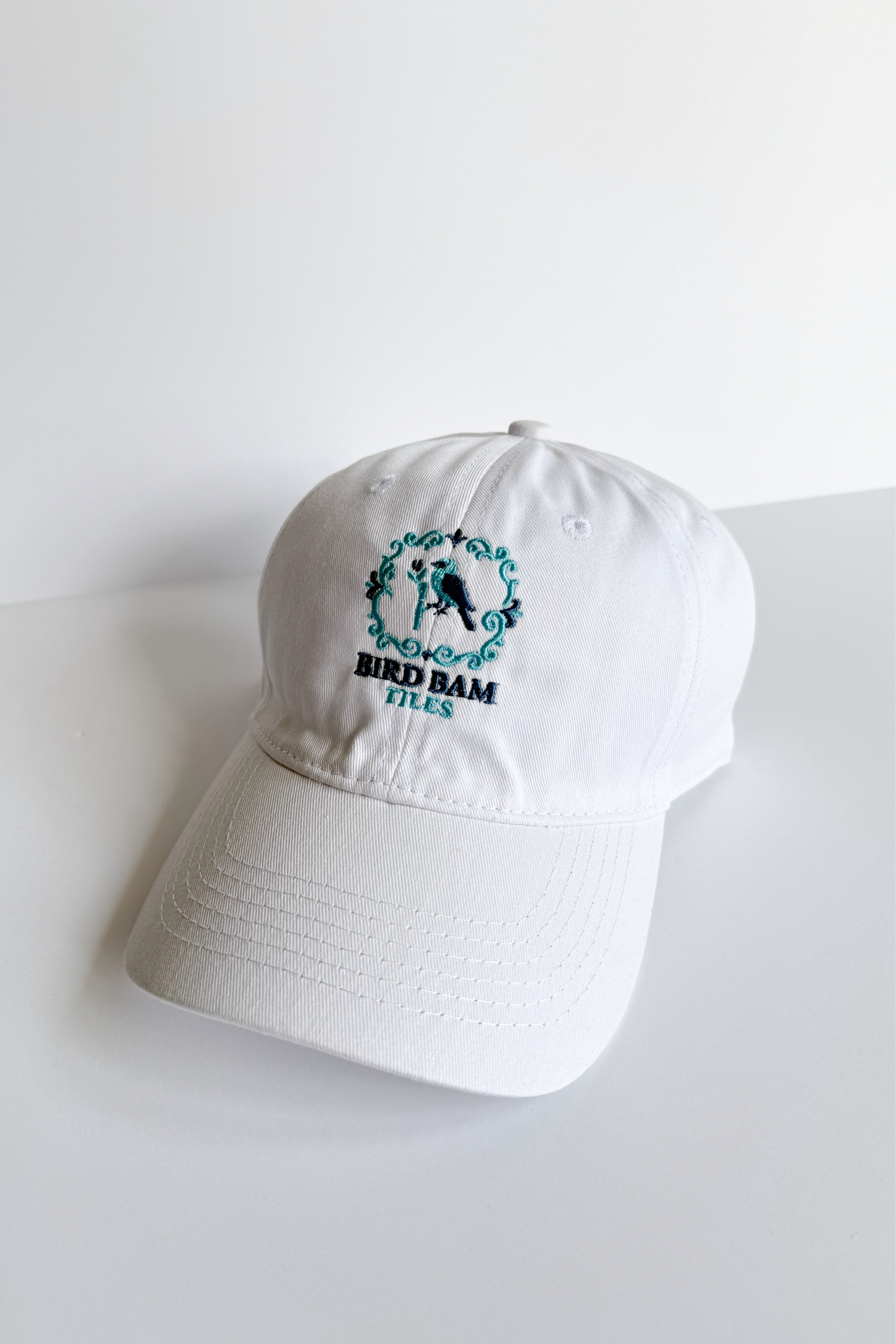 White baseball hat embroidered with 2-toned blue Bird Bam Tiles logo on a white background