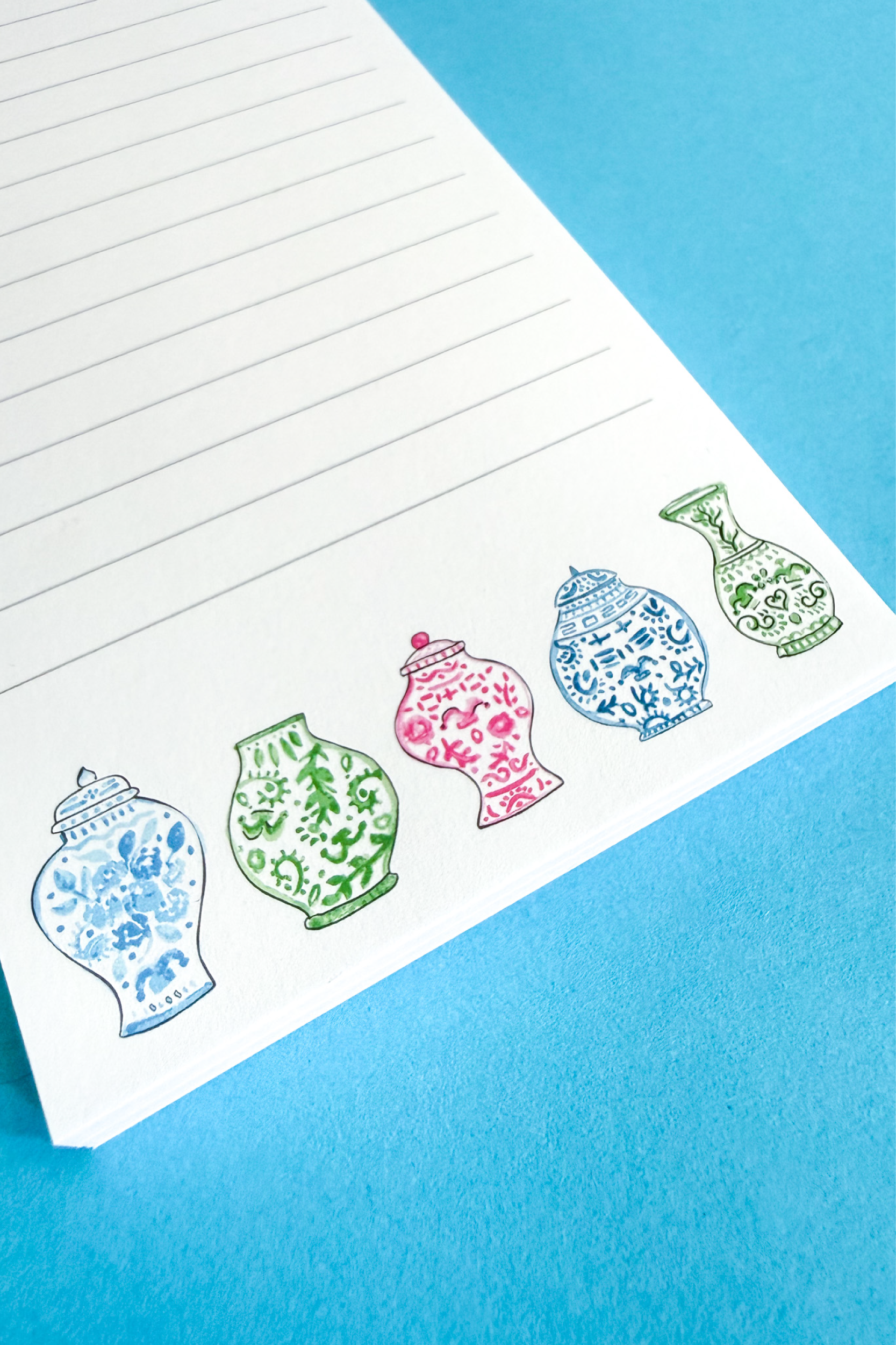 Upclose details of a lined notepad with 5 ginger jars in blues, greens, and pinks at the bottom of the notepad