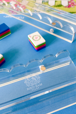 Clear acrylic scallop rack with an etched Bird Bam Tiles logo on a colorful game mat background