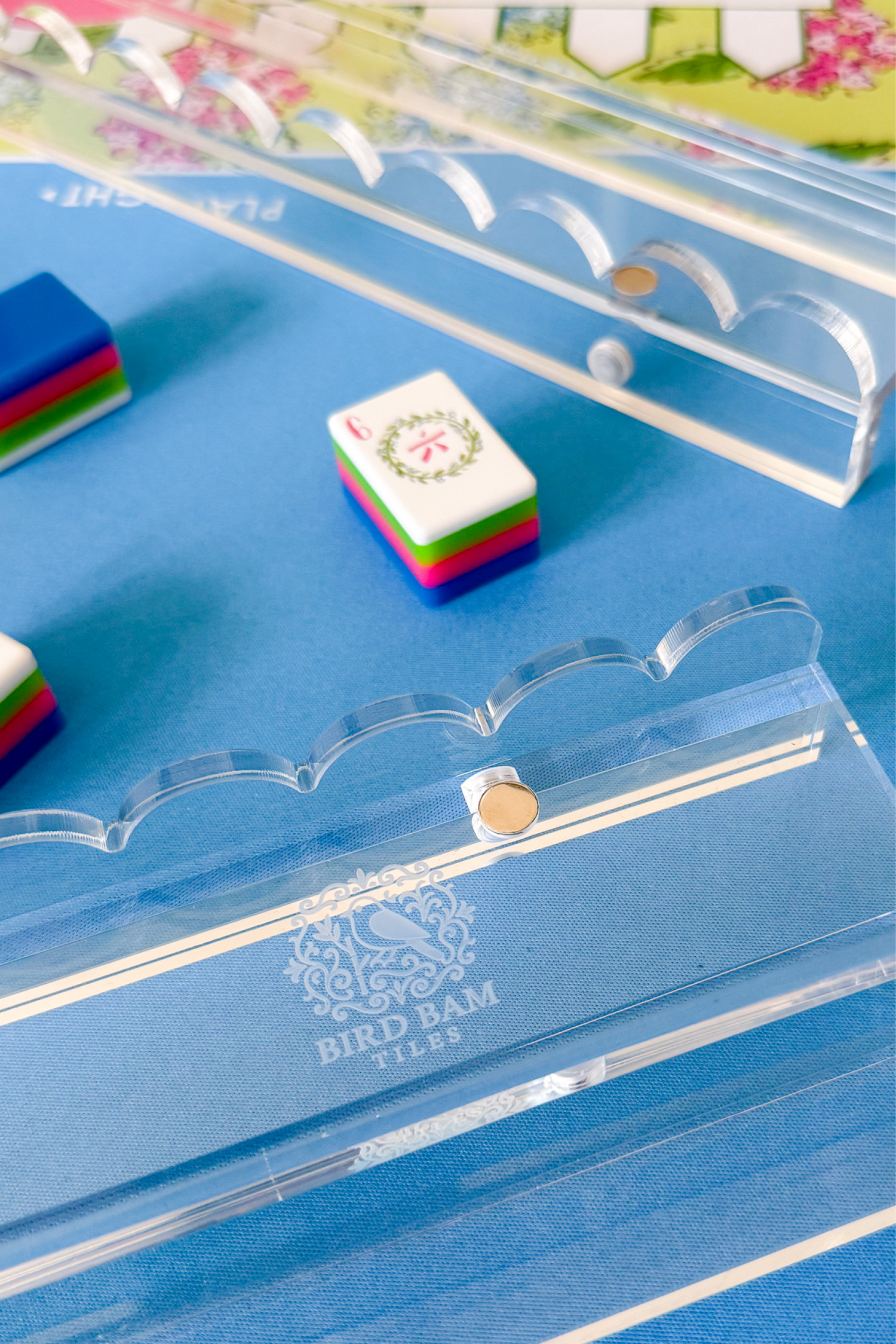 Clear acrylic scallop rack with an etched Bird Bam Tiles logo on a colorful game mat background